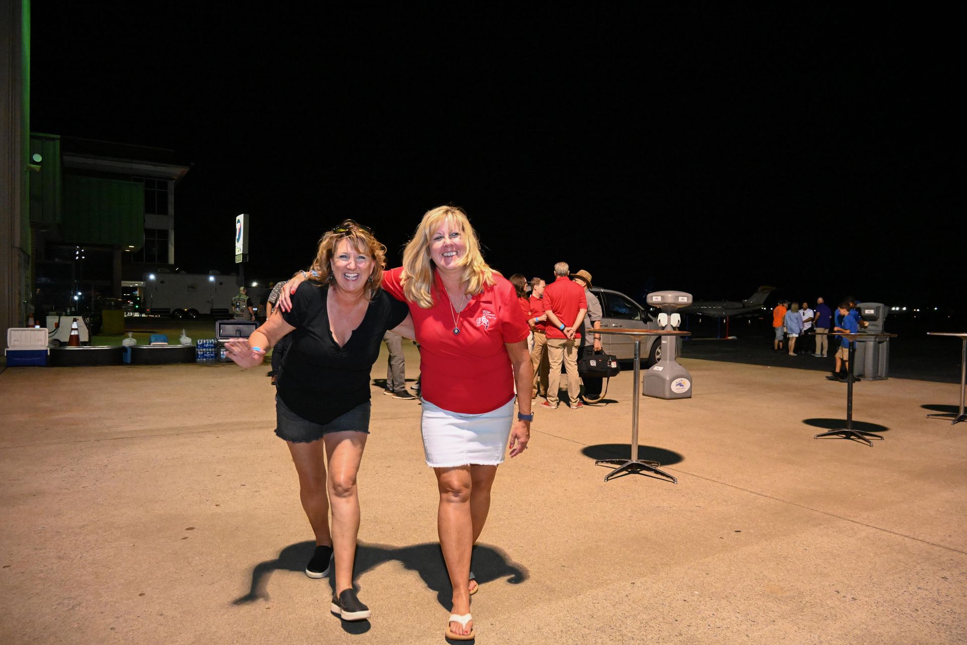 Two women are walking in a parking lot at night.
