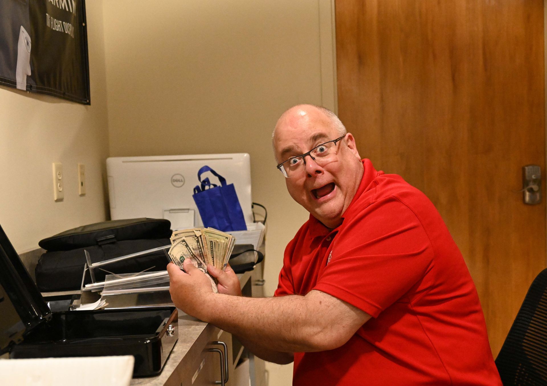 A man wearing glasses and a red shirt is sitting at a desk.