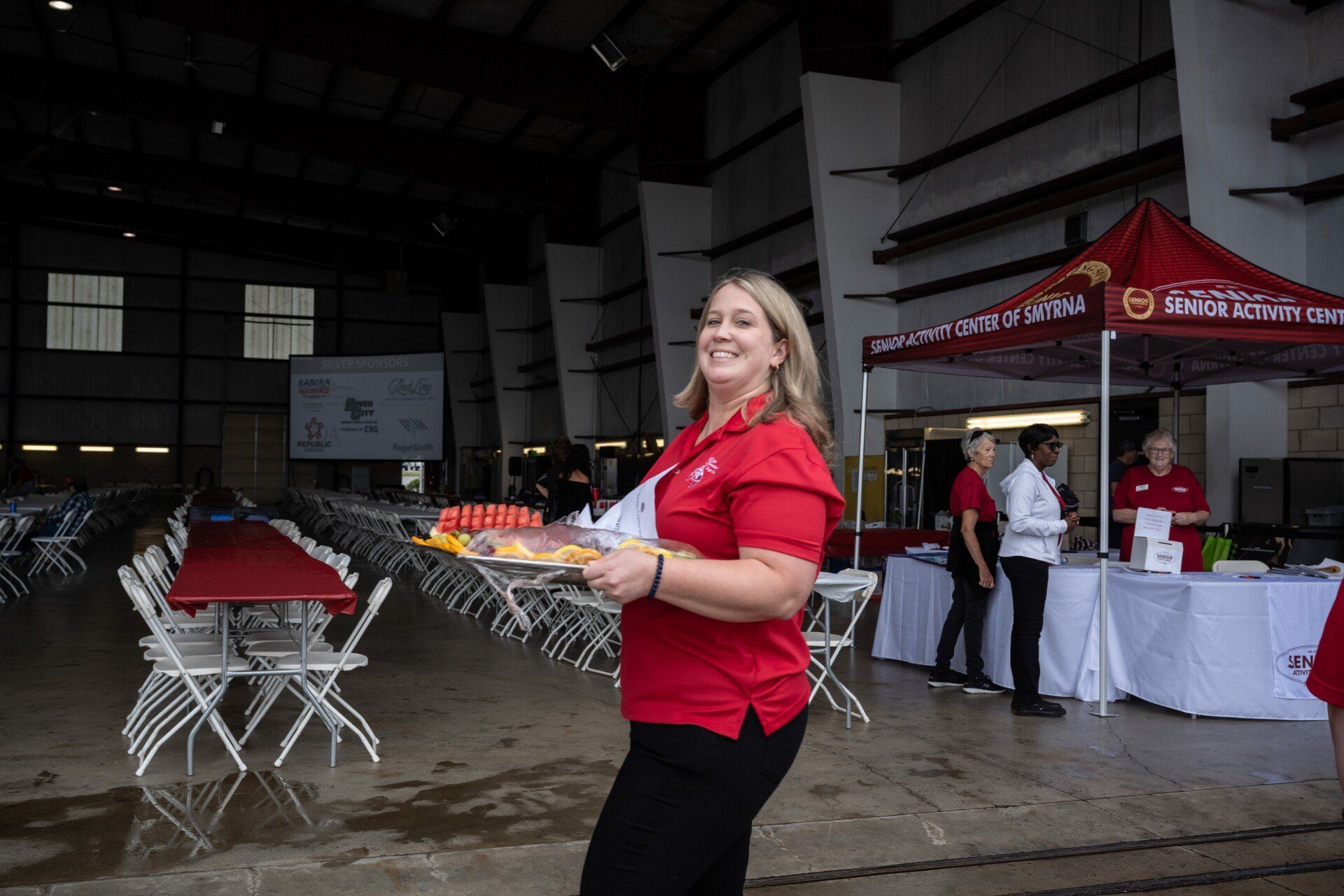 A woman in a red shirt is holding a plate of food.