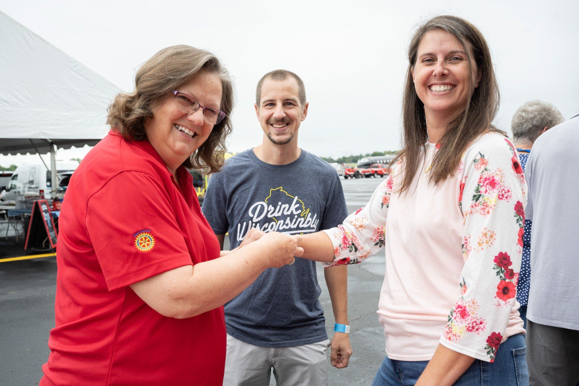 A woman is shaking hands with a man and a woman in a parking lot.
