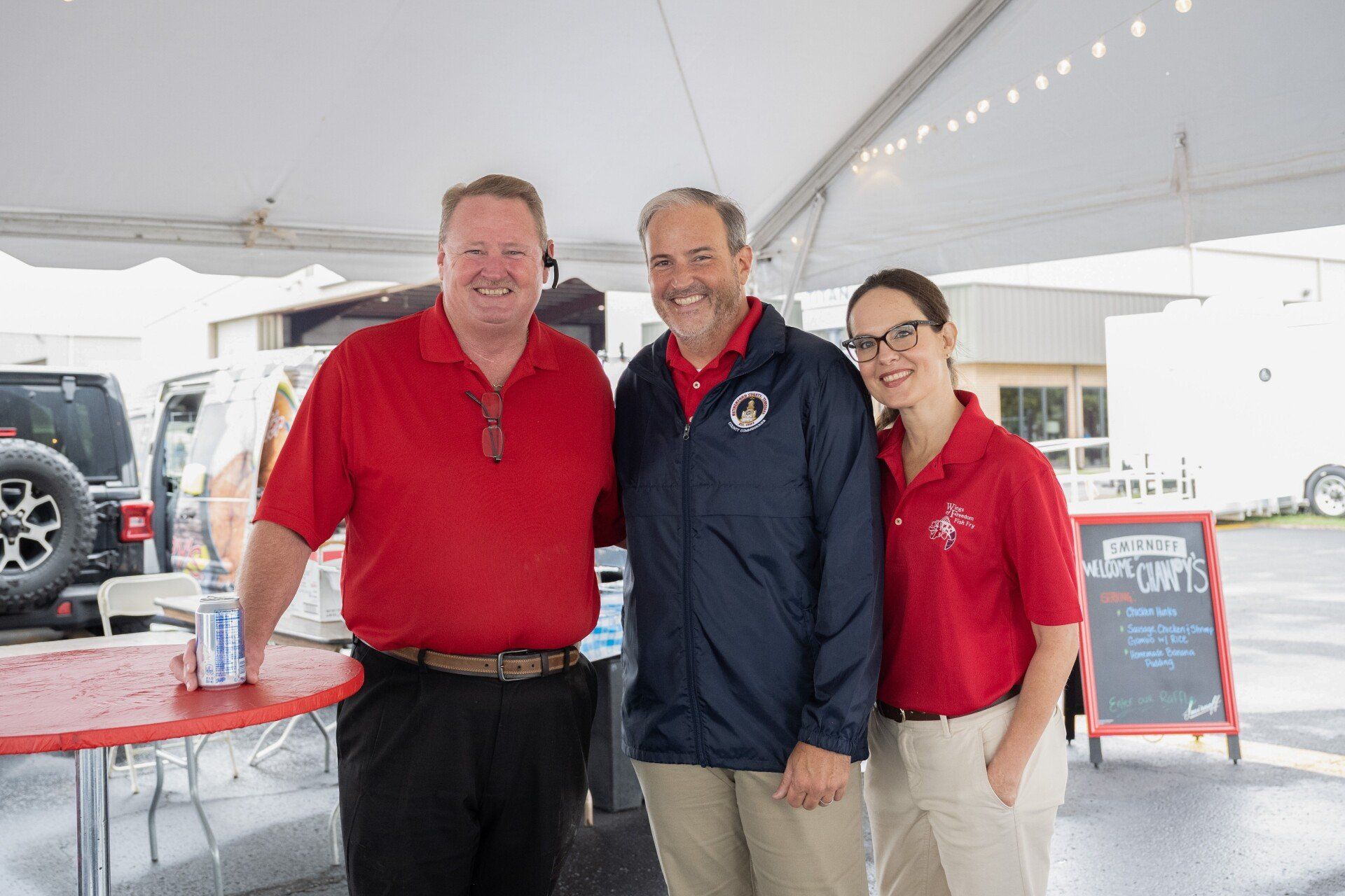 Three people are posing for a picture under a tent.