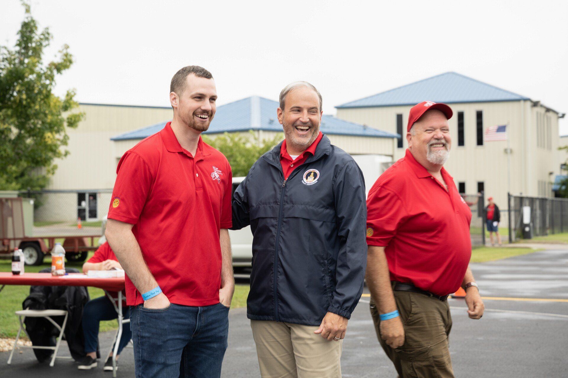 Three men in red shirts are standing next to each other in front of a building.