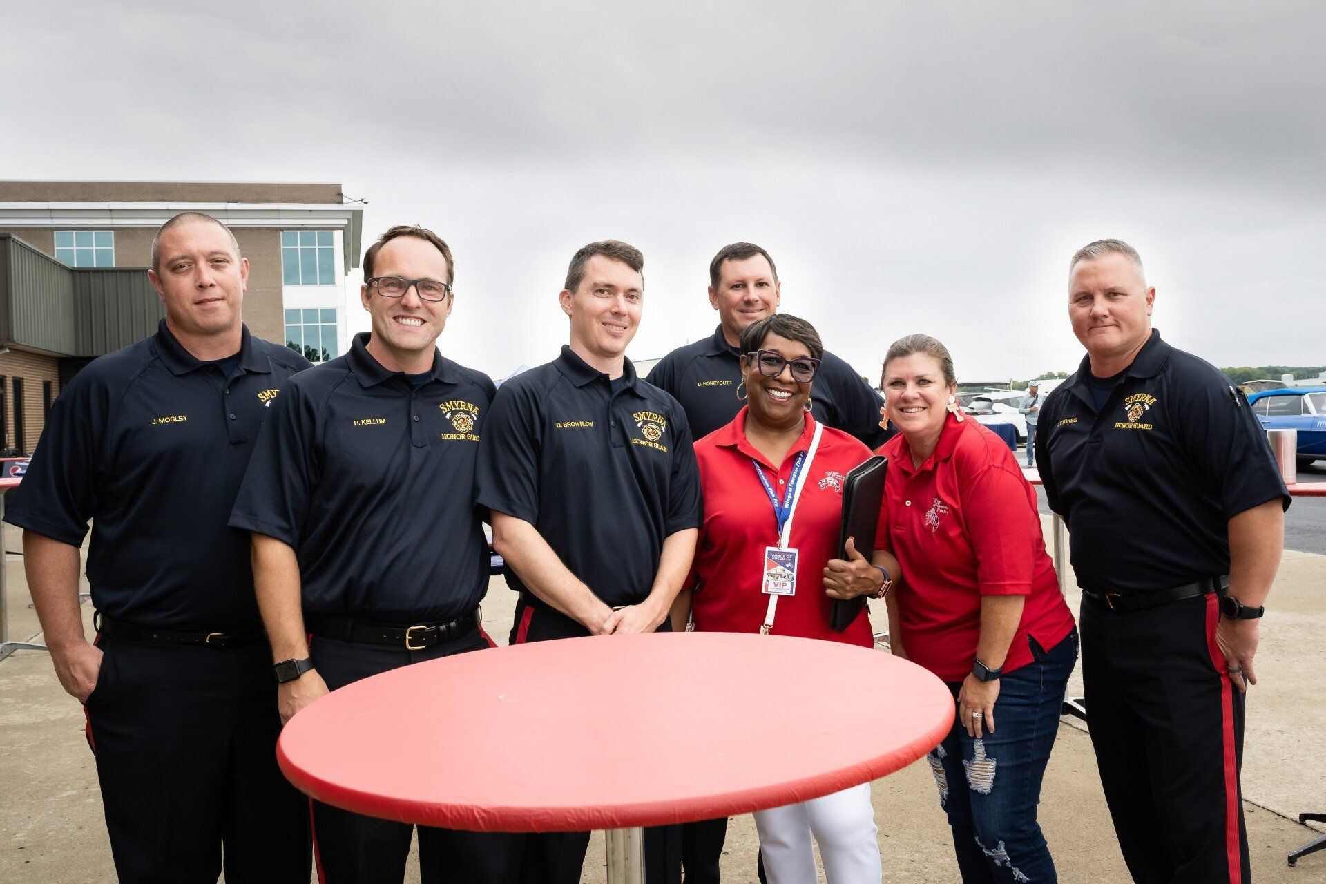 A group of people standing around a red table.