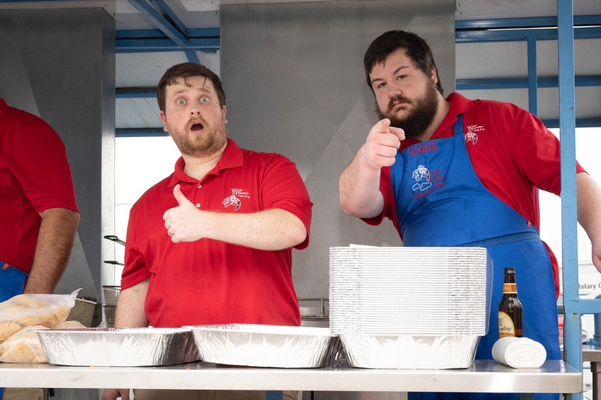 Two men in red shirts and blue aprons are giving a thumbs up.