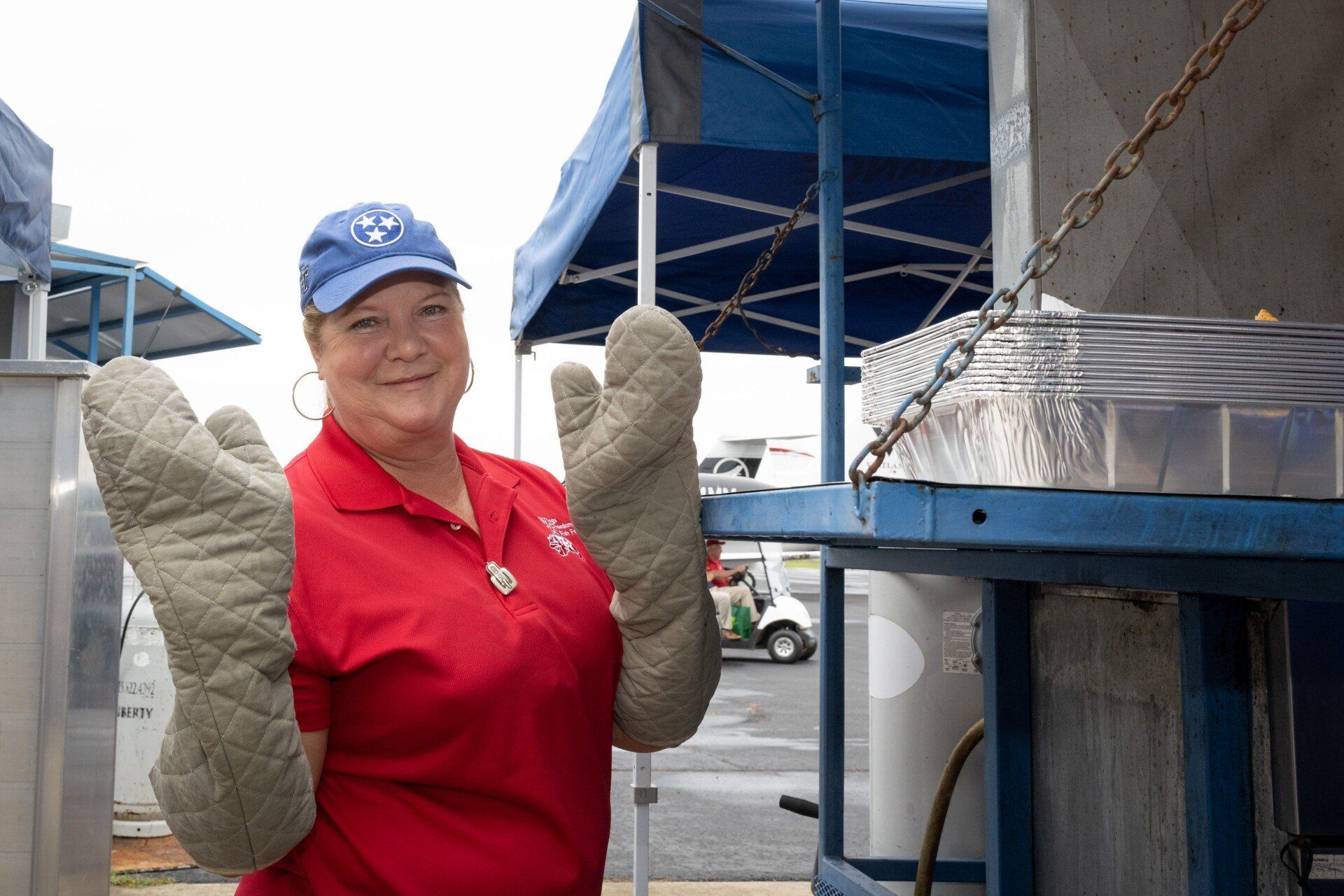 A woman in a red shirt is wearing oven mitts