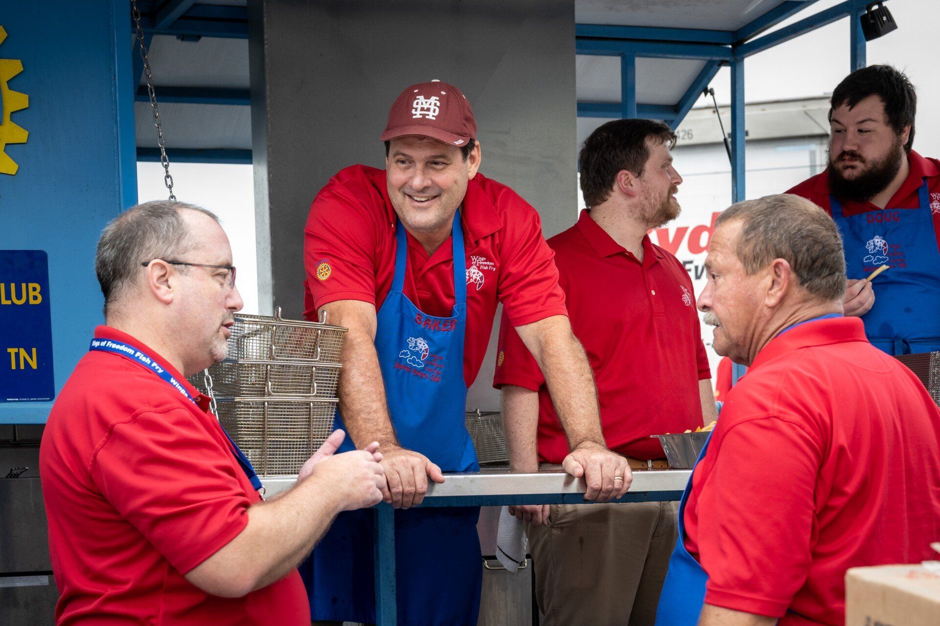 A group of men in red shirts and blue aprons are talking to each other.