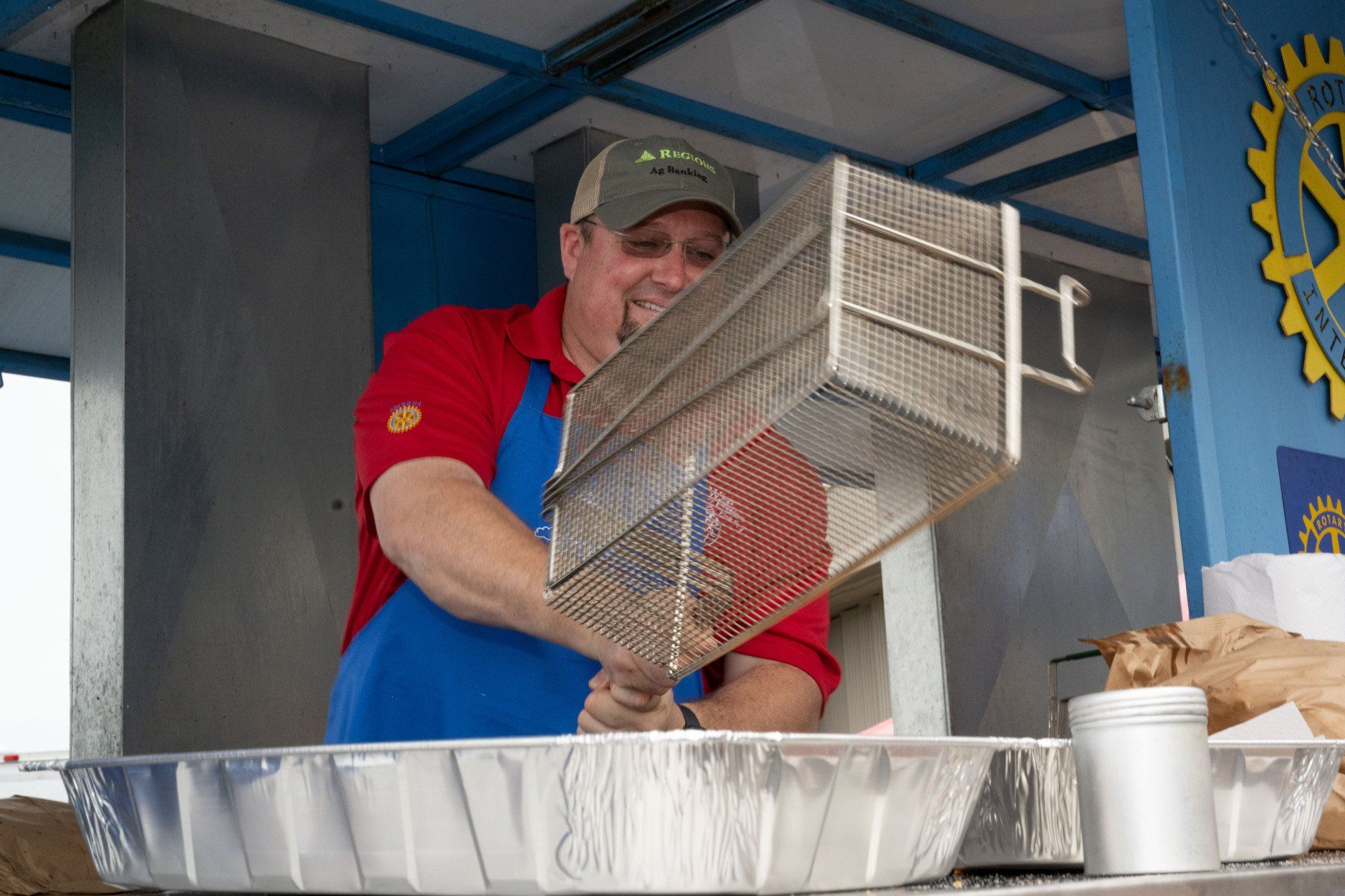A man in a red shirt and blue apron is holding a wire basket