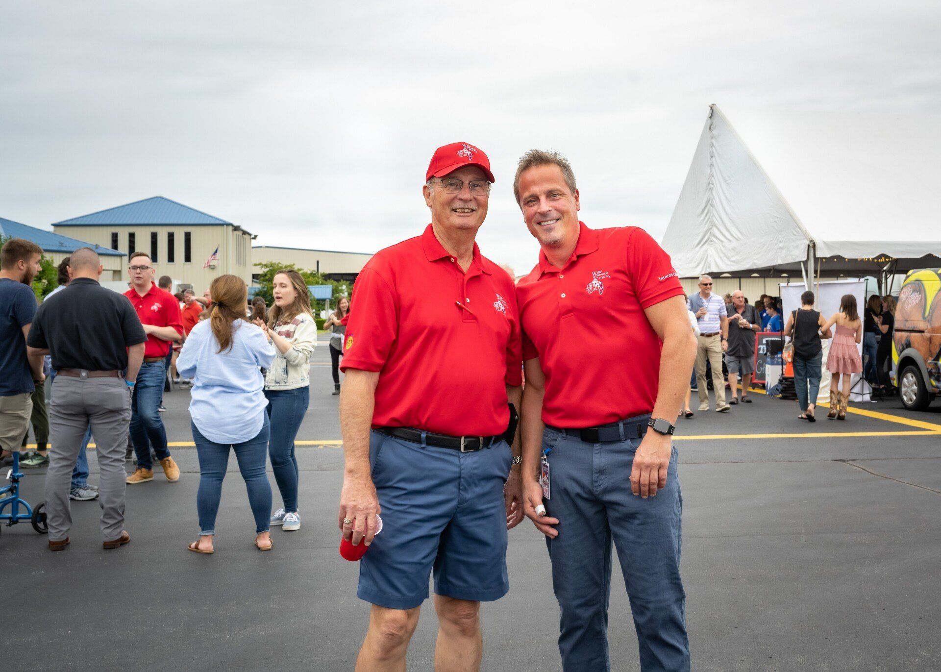 Two men in red shirts are standing next to each other in a parking lot.