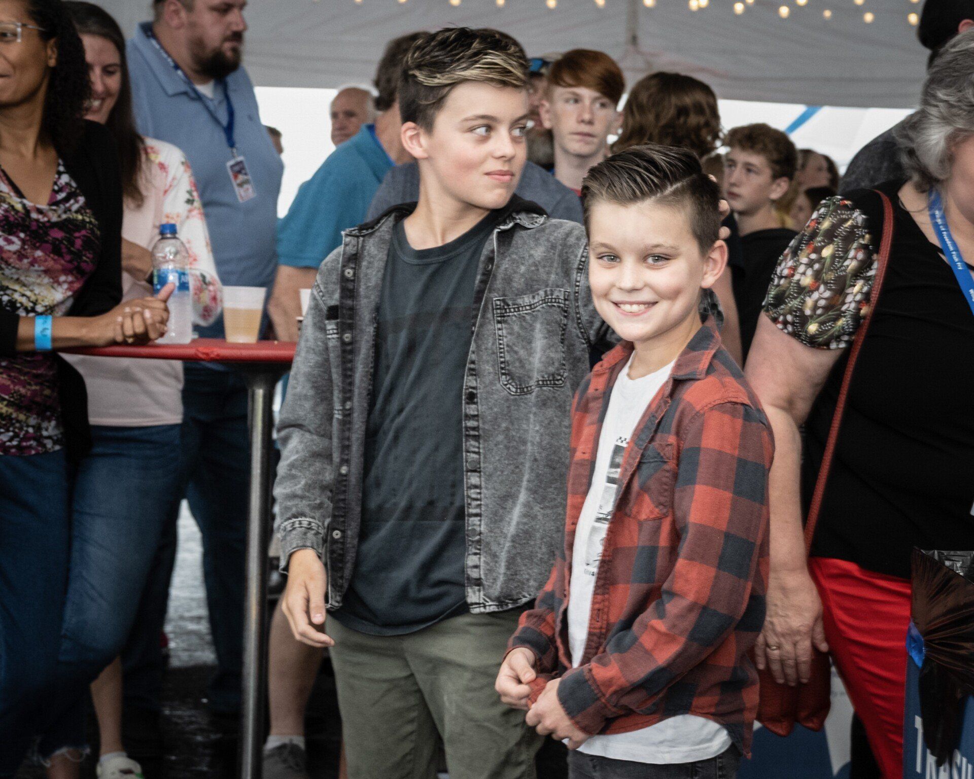 Two young boys are standing in front of a crowd of people.