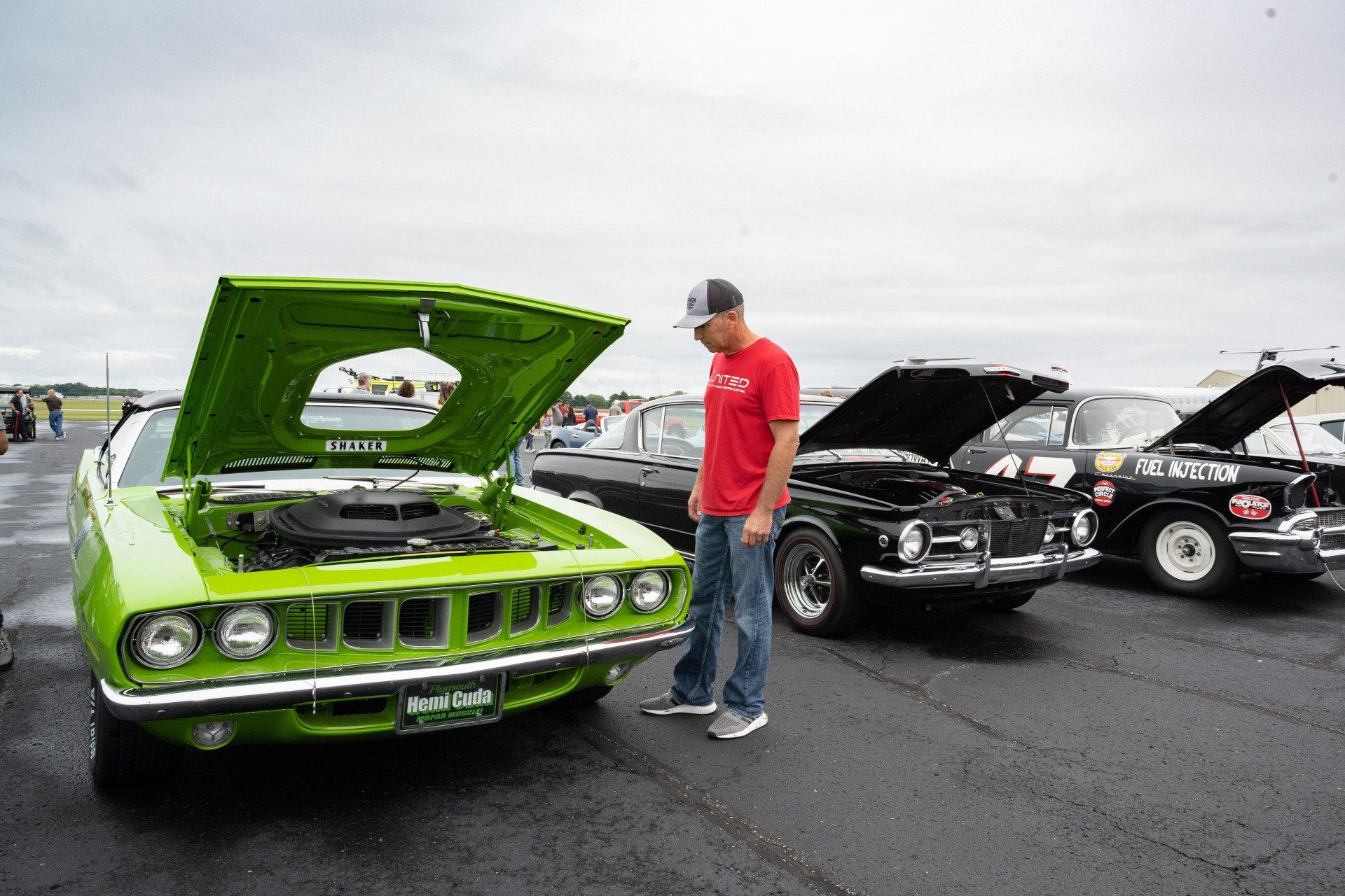A man is looking under the hood of a green car.
