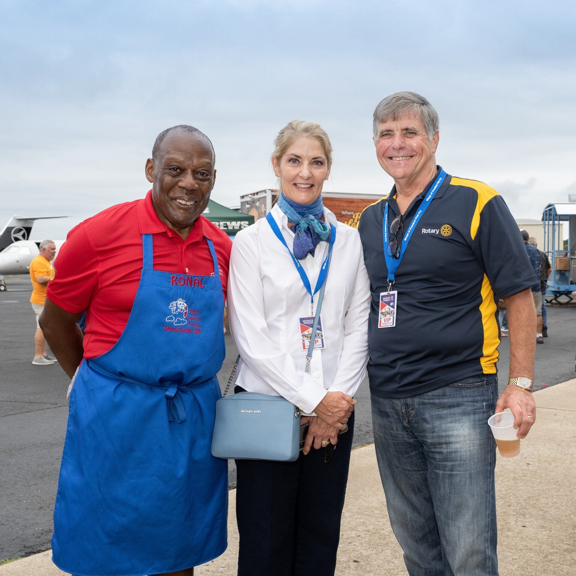 Three people posing for a picture with one wearing a blue apron