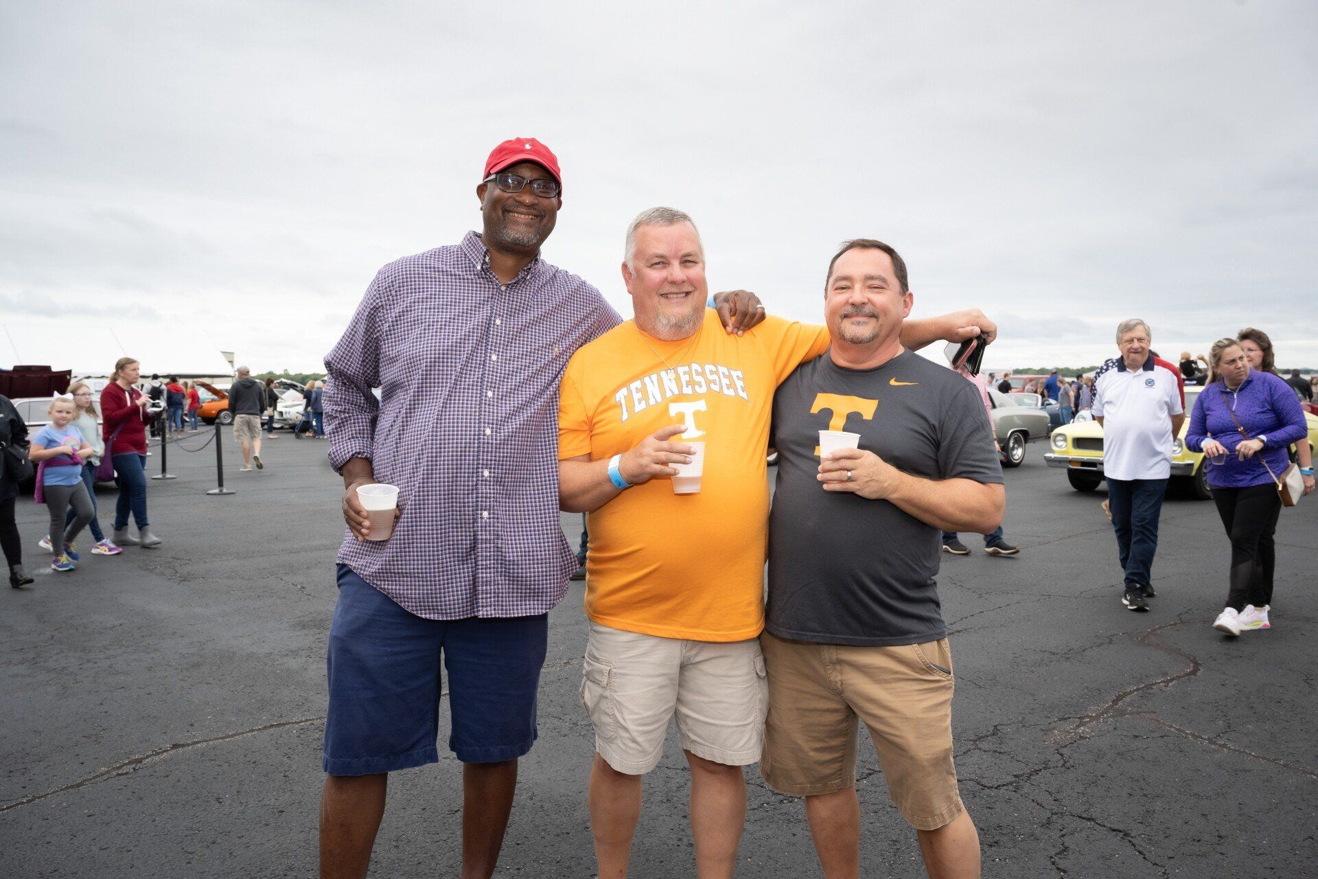 Three men are posing for a picture in a parking lot.