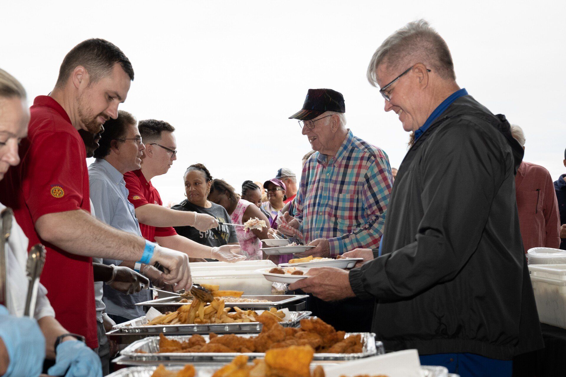 A group of people are standing around a buffet line eating food.