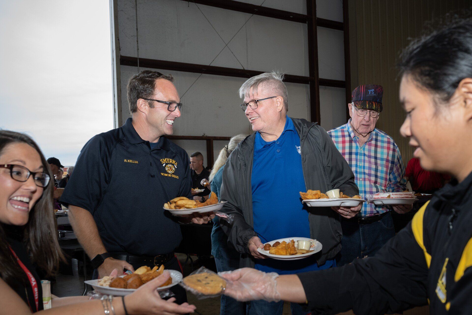 A group of people are standing around a table holding plates of food.