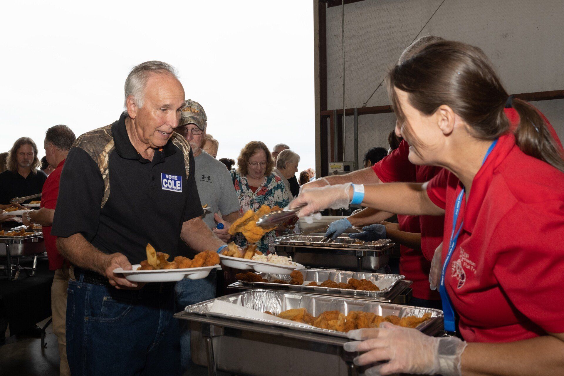 A woman in a red shirt is serving food to a man in a black shirt.