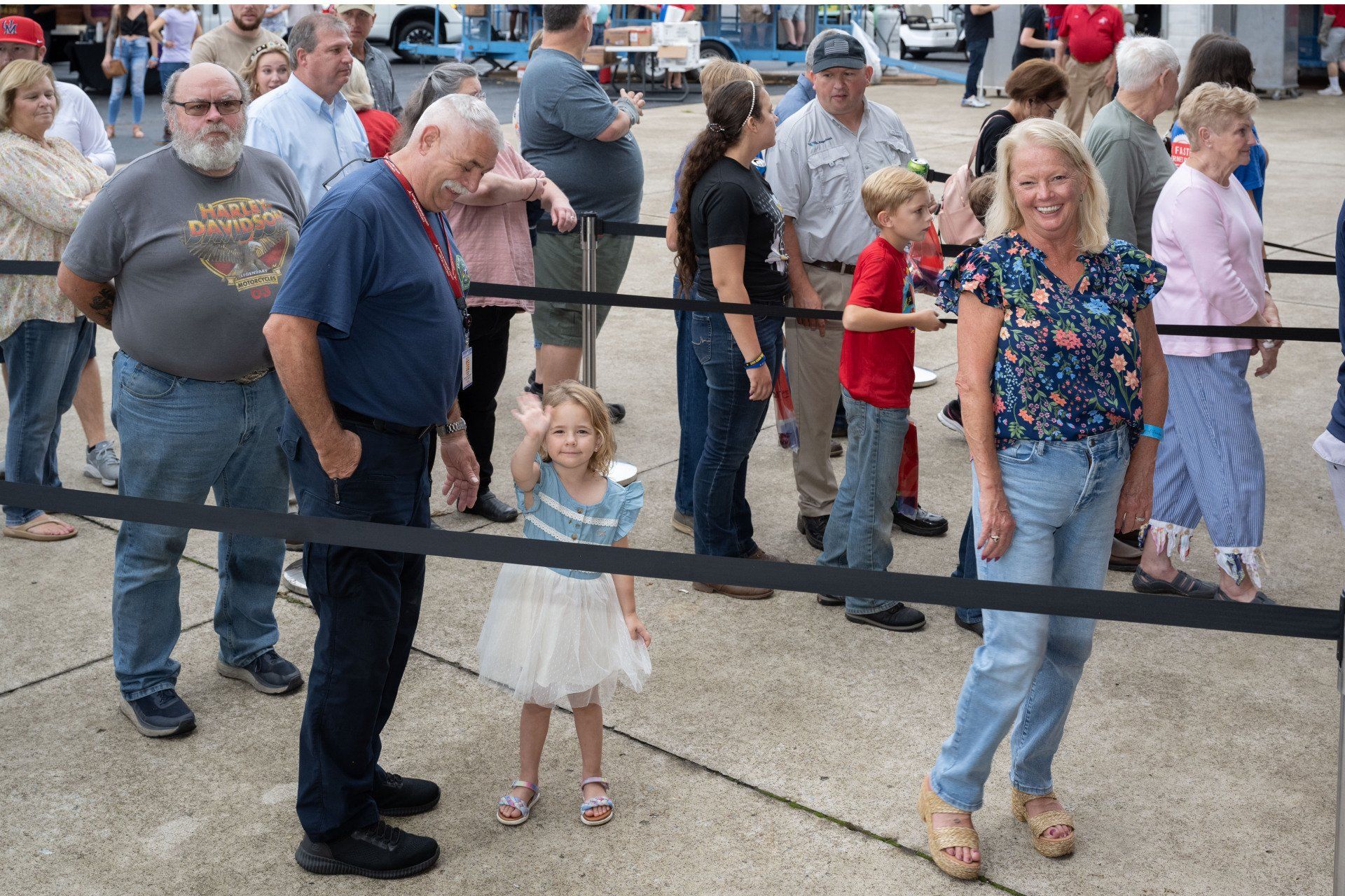 A group of people are standing in a line behind a black barrier.