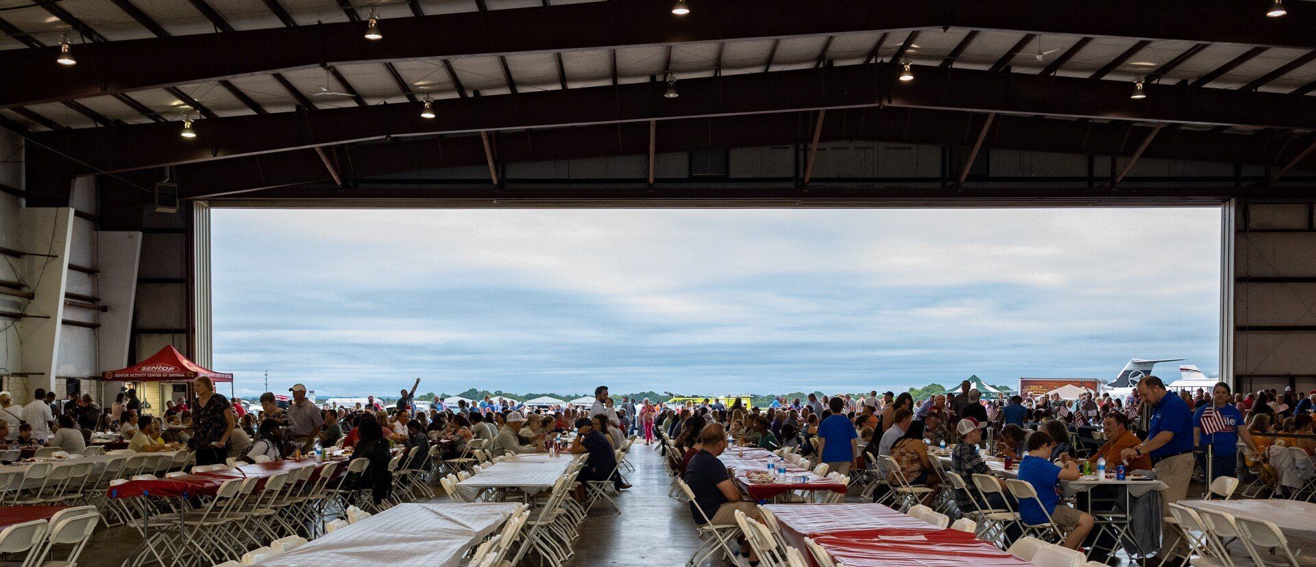 A large group of people are sitting at tables in an airplane hangar.