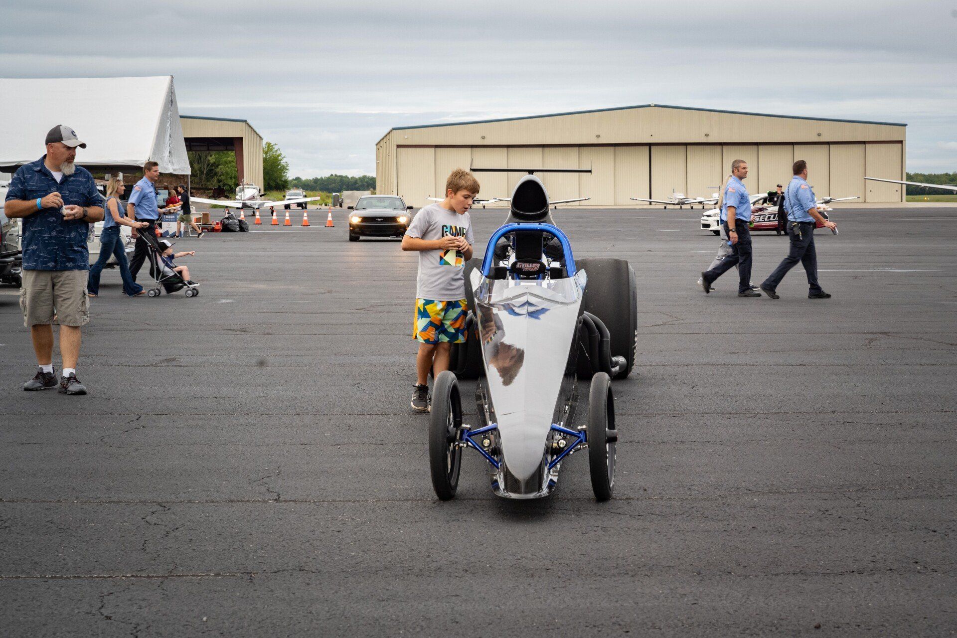 A group of people are standing around a race car on a runway.