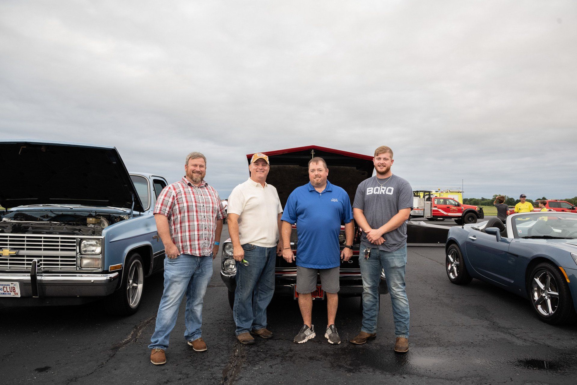 A group of men are standing in front of a car with the trunk open.