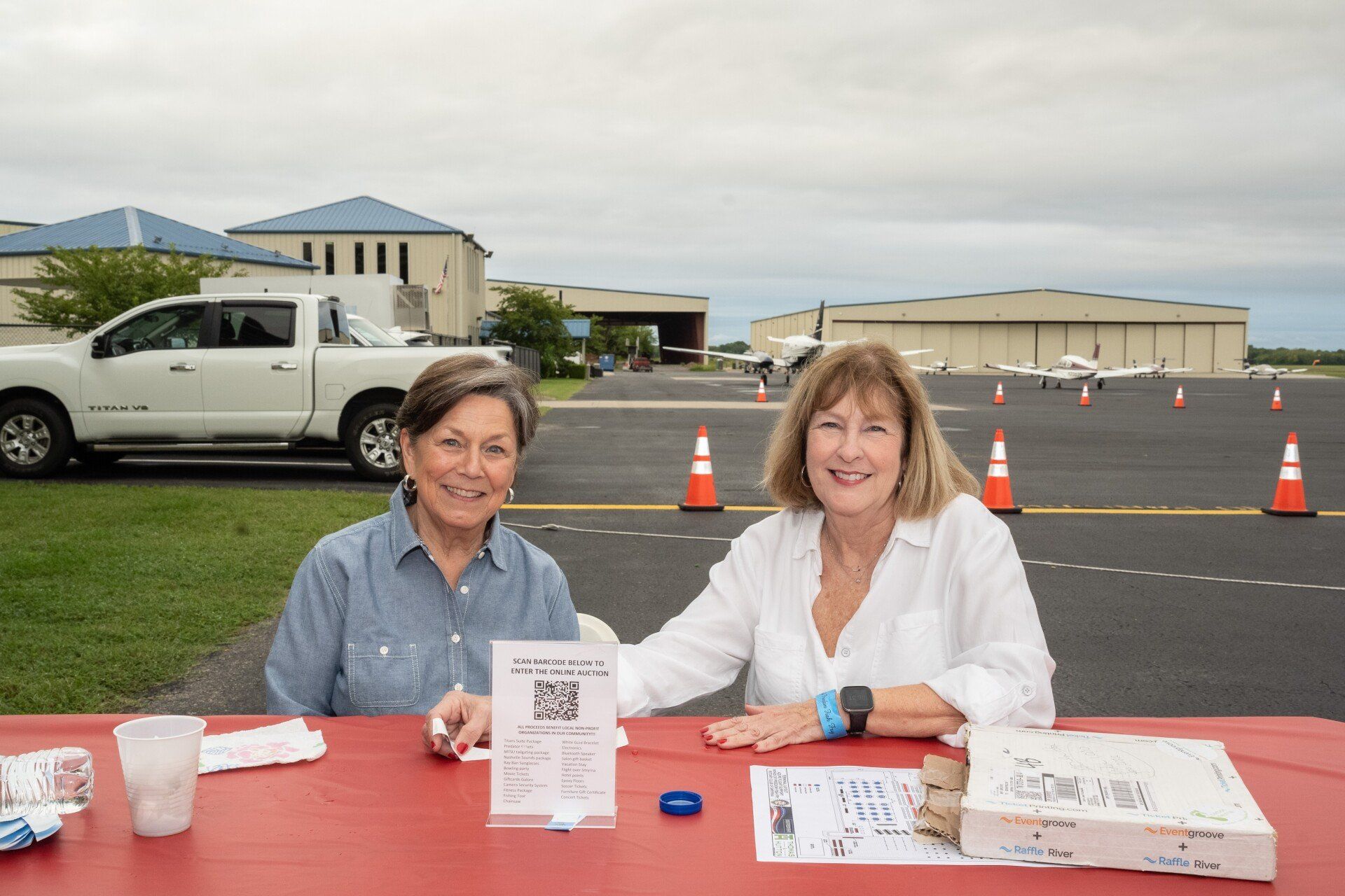 Two women are sitting at a table in a parking lot.
