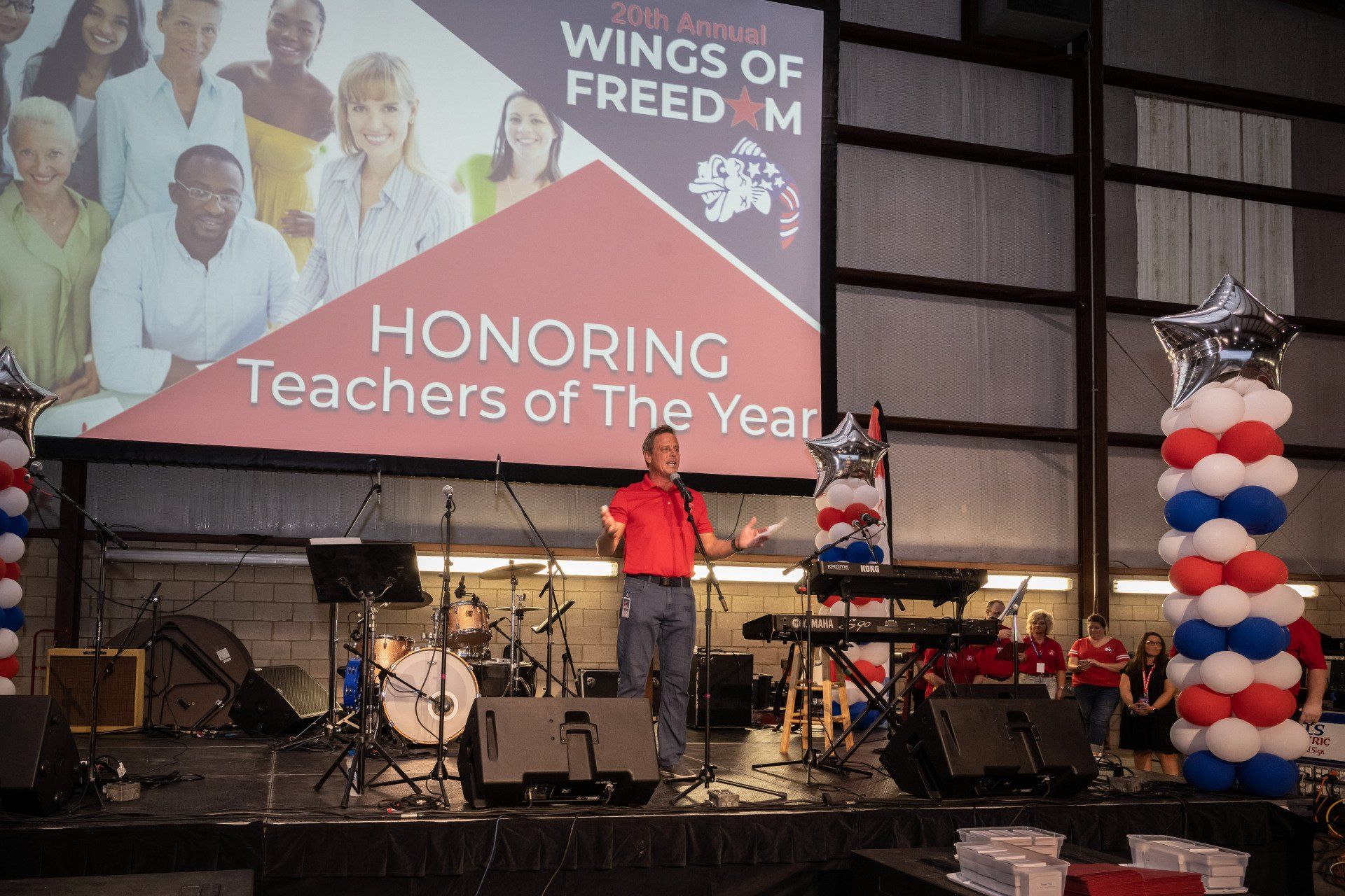 A man is standing on a stage in front of a large screen that says honoring teachers of the year.
