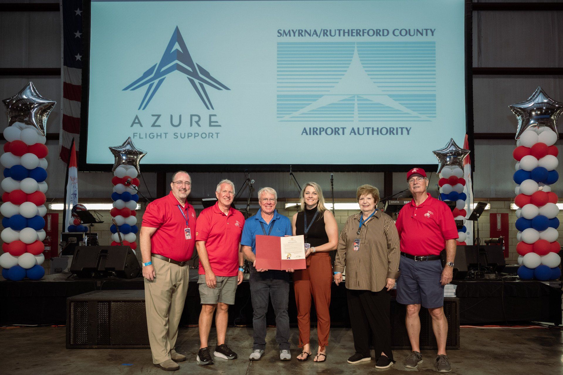 A group of people are standing in front of a large screen.