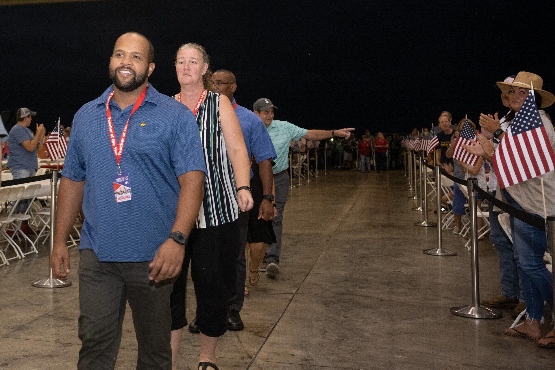 A man and a woman are standing in a line with people holding american flags.