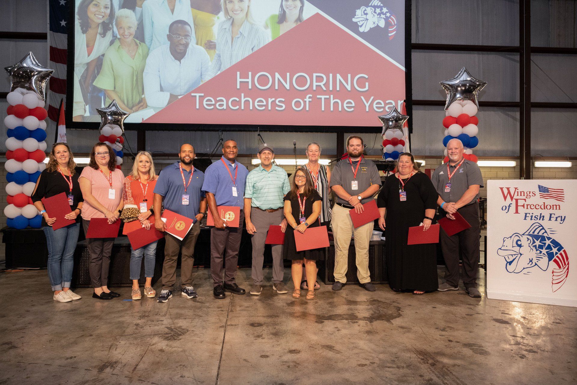 A group of people are standing in front of a screen that says honoring teachers of the year.