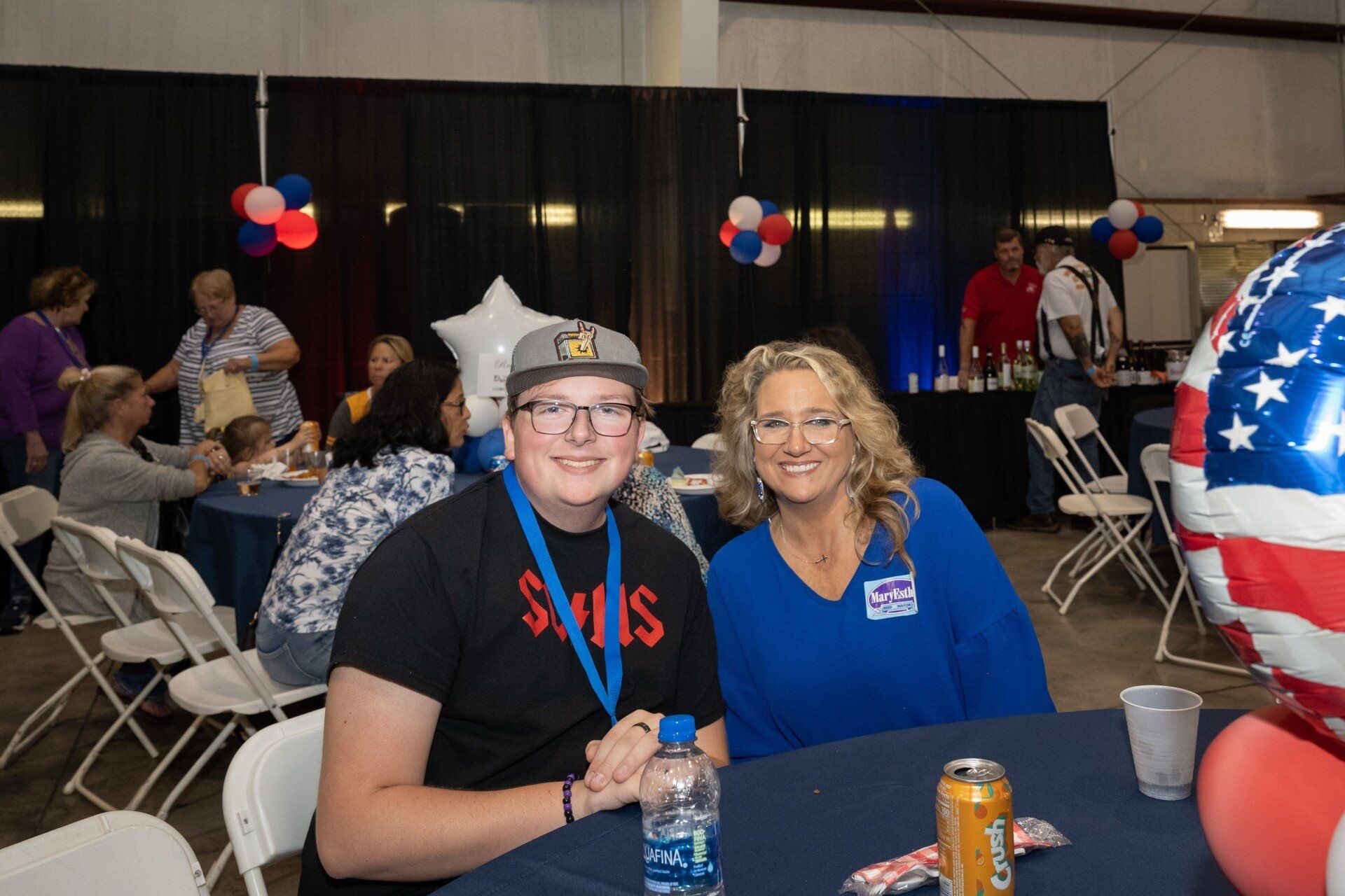 A man and a woman are sitting at a table in a room with balloons.