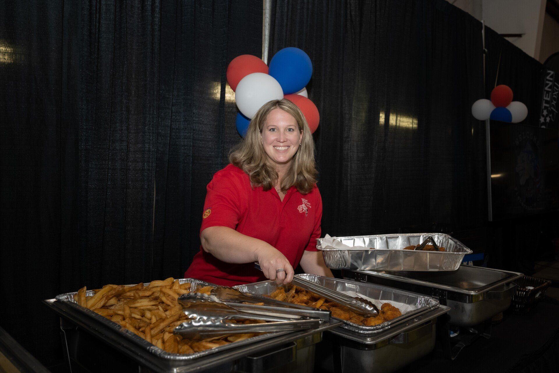 A woman in a red shirt is serving food at a buffet table.