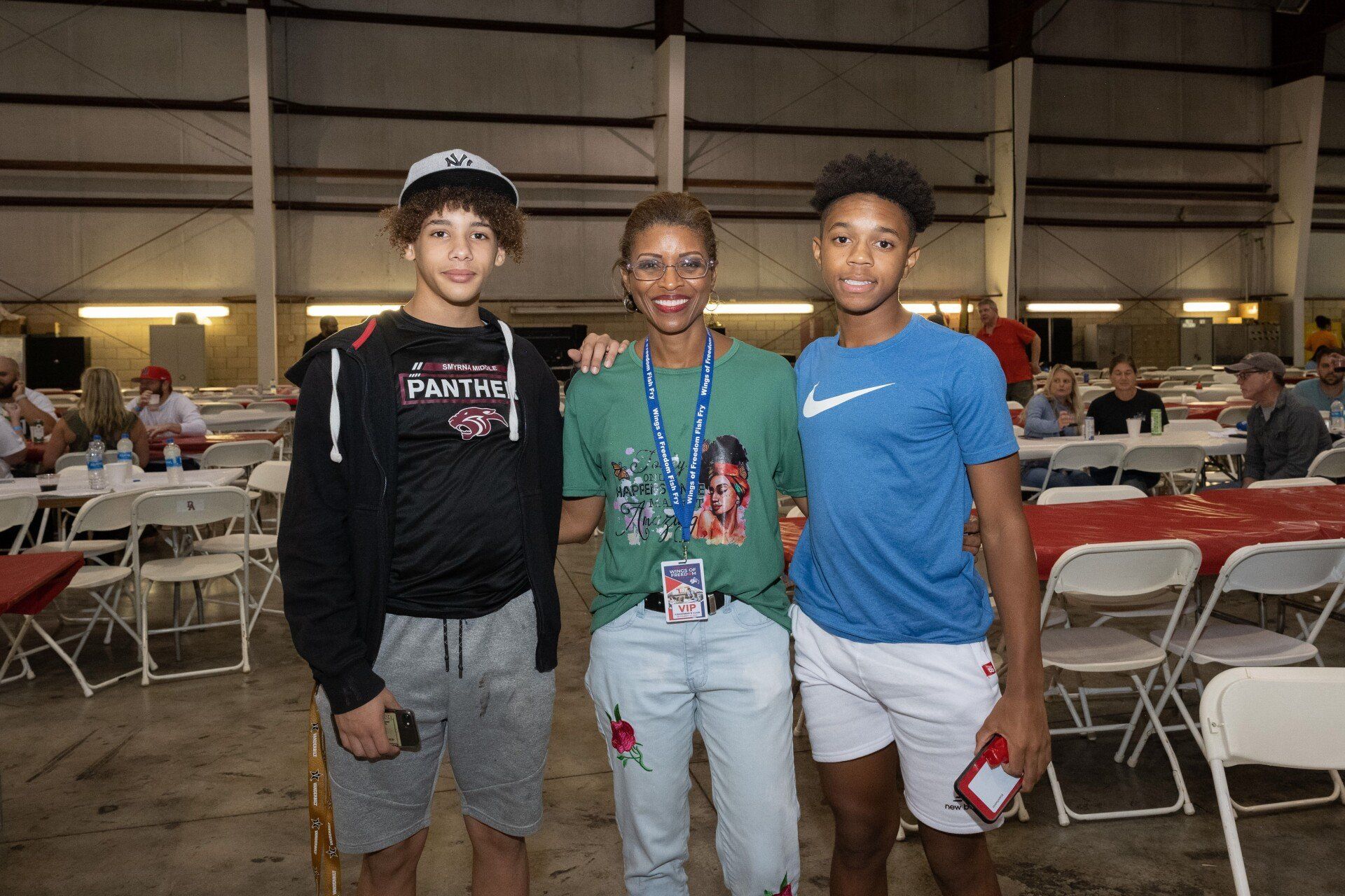 Three people are posing for a picture in a room with tables and chairs.