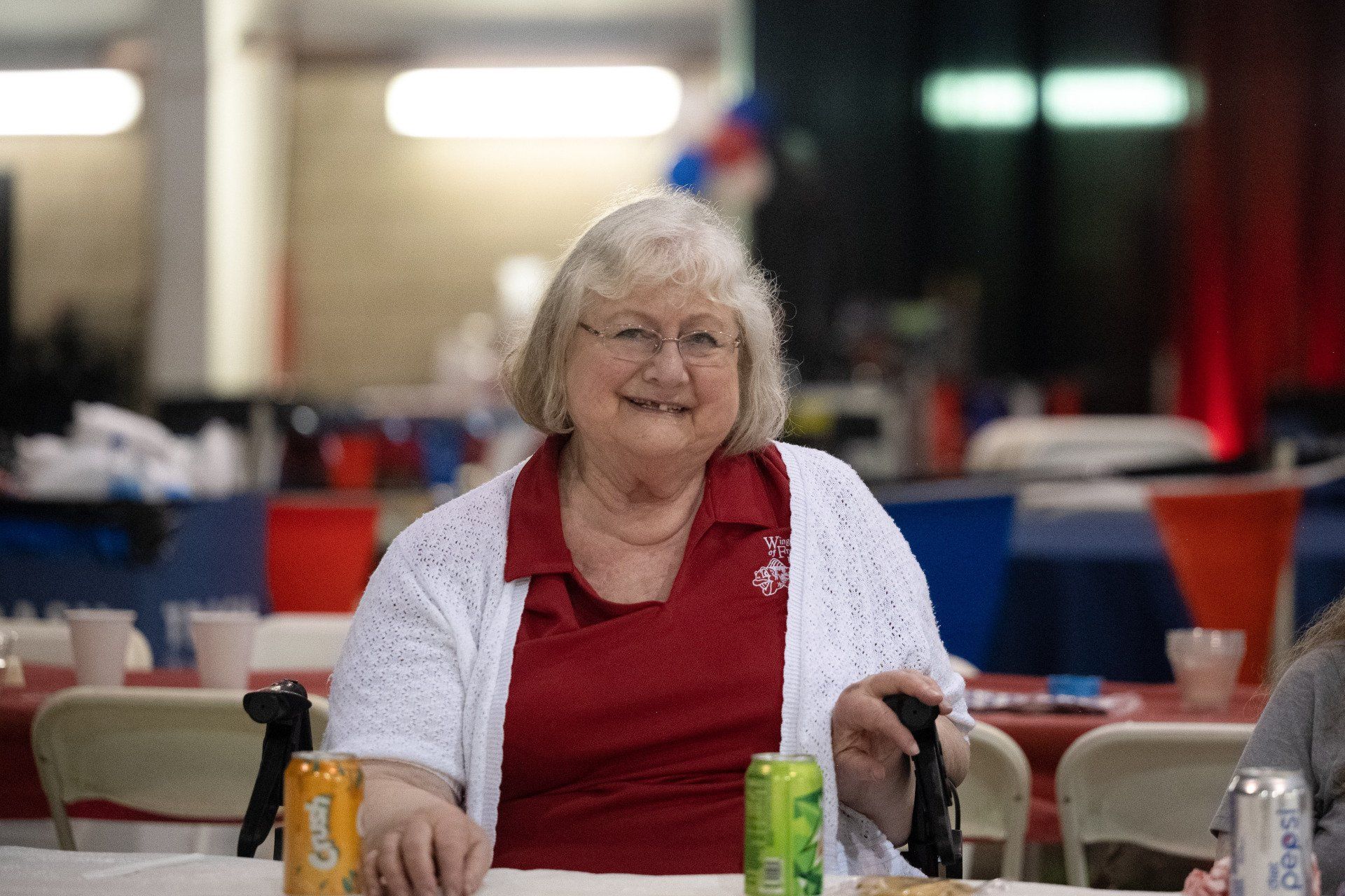 An elderly woman is sitting at a table with a can of soda.