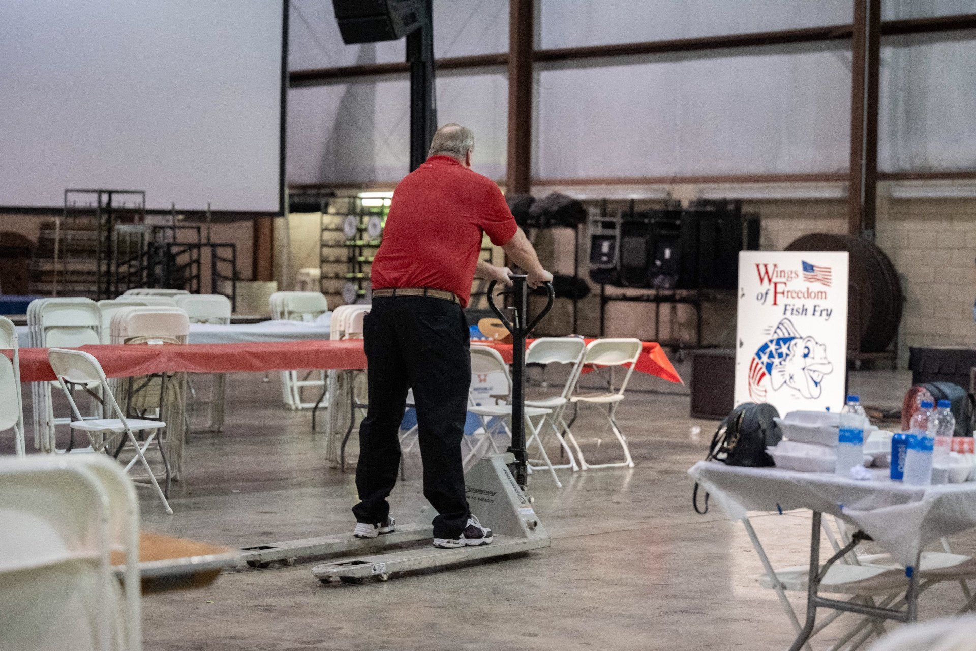 A man is pushing a pallet truck in a room with tables and chairs