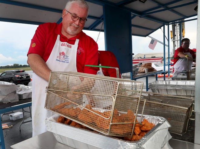 A man in an apron is holding a basket of fried food.