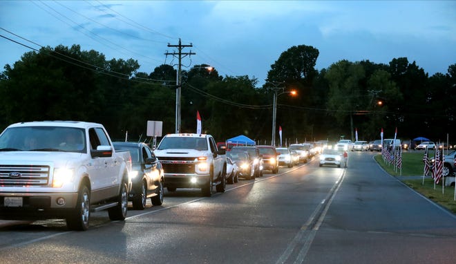 A long line of cars are driving down a street at night.