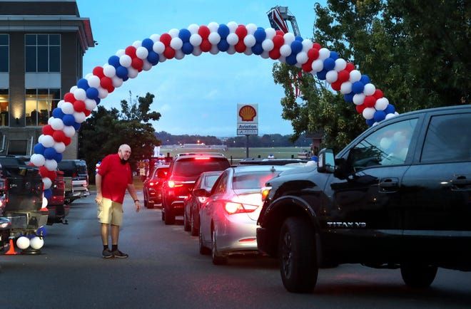 A row of cars are parked under a red white and blue balloon arch