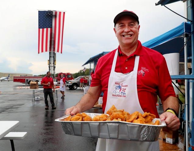 A man in a red shirt and apron is holding a tray of food