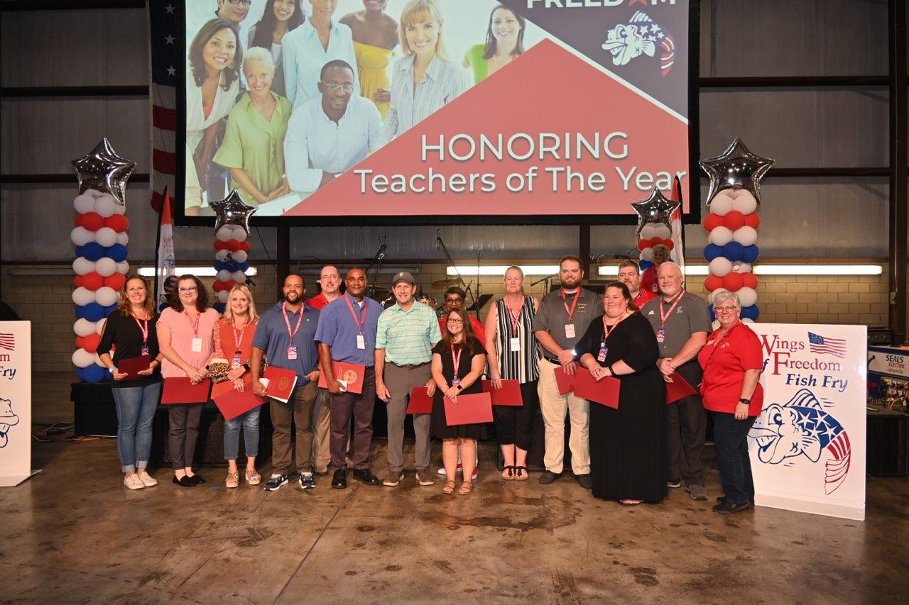 A group of people are standing in front of a large screen that says honoring teachers of the year.