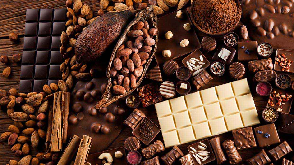 Surtido de barras de chocolate, granos de cacao y nueces sobre una superficie de madera.