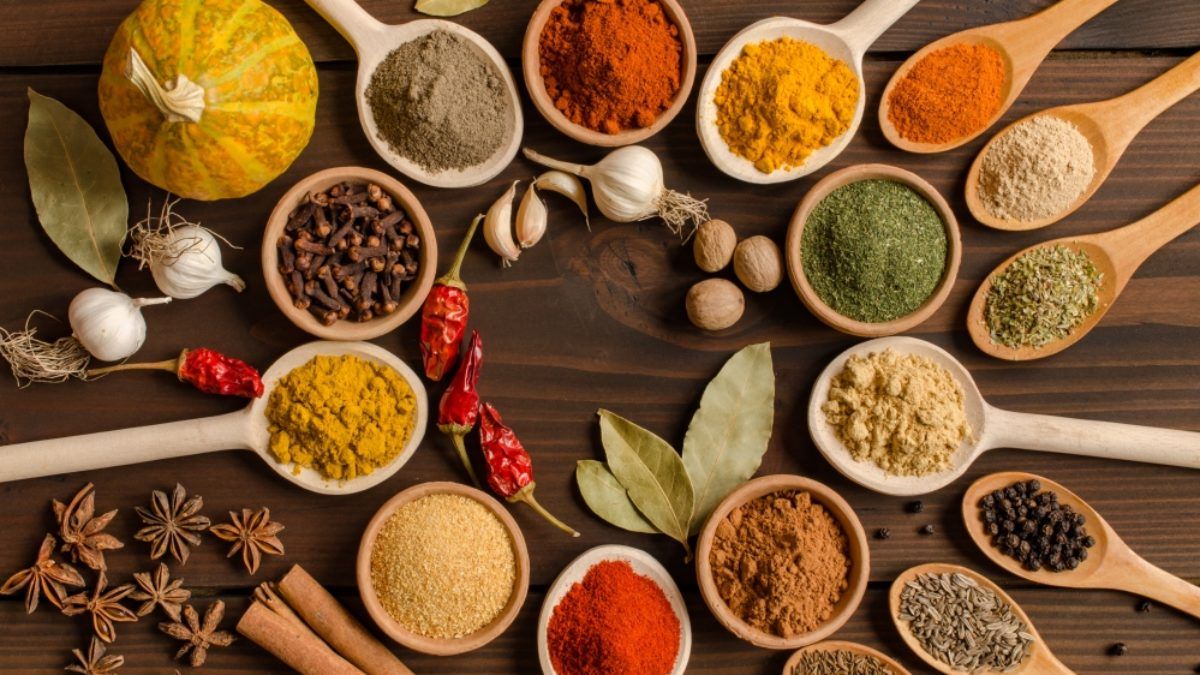 Varias especias coloridas en cuencos y cucharas de madera sobre una superficie de madera.