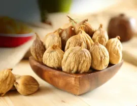 Higos secos en un cuenco de madera, primer plano. Frutos marrones con textura. Fondo claro.