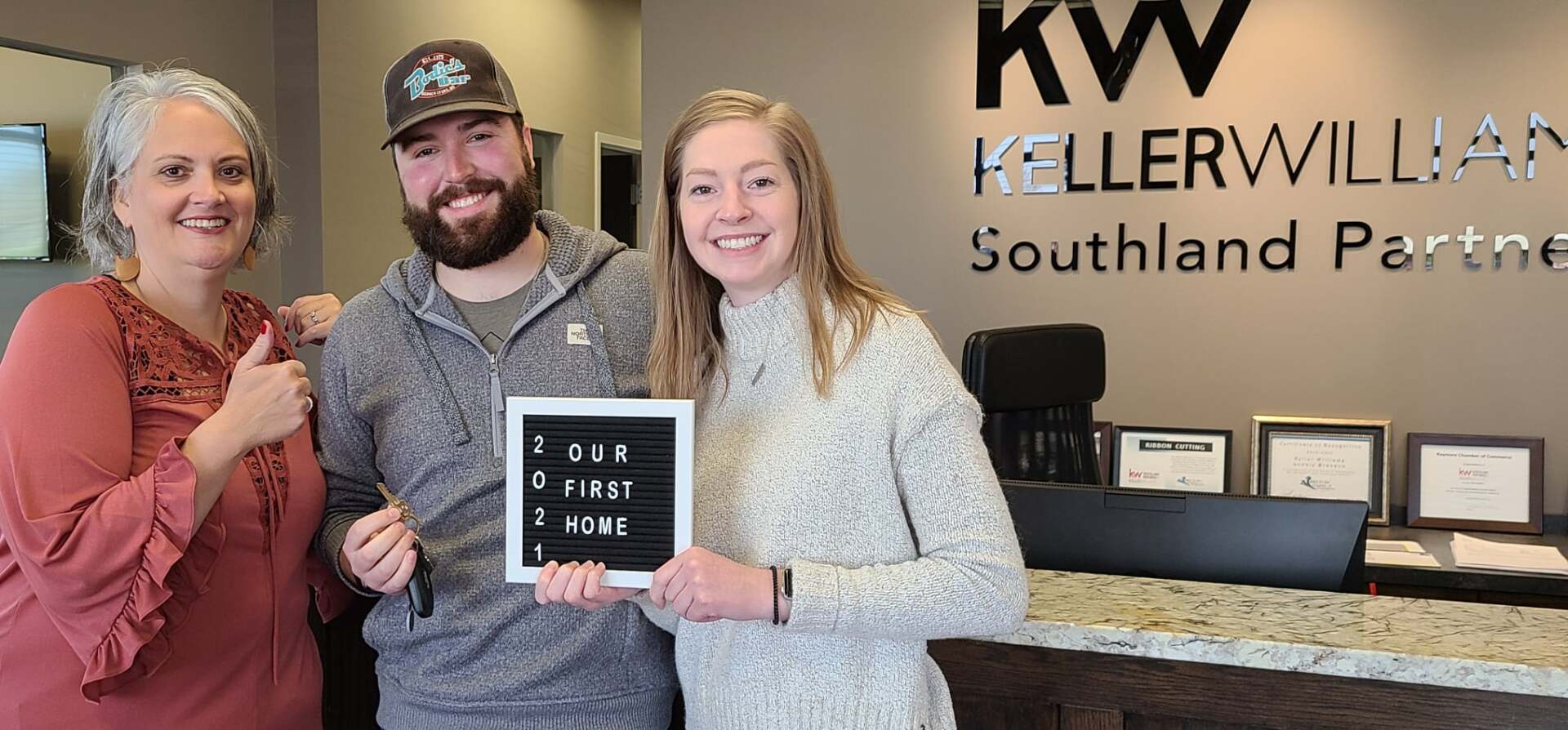 A man and two women are posing for a picture in front of a kellerwilliams sign.