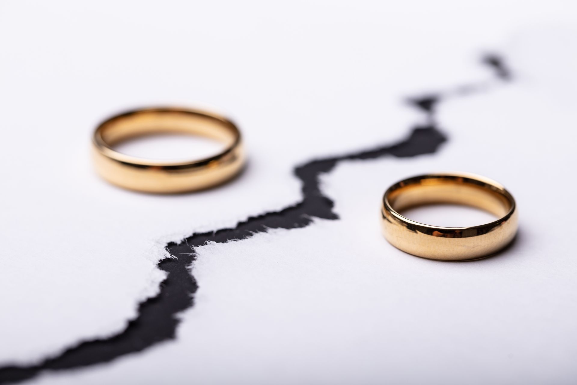 Two gold wedding rings are sitting on top of a cracked piece of paper.