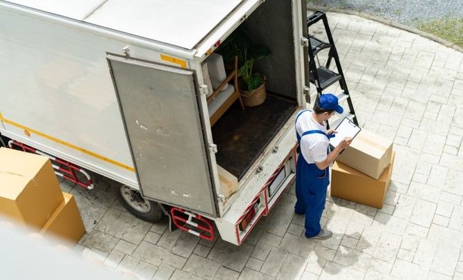 Delivery worker loading cardboard boxes into a truck from a paved loading area