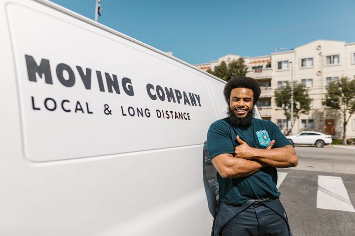Moving company van with logo beside a smiling worker standing outdoors in a parking lot