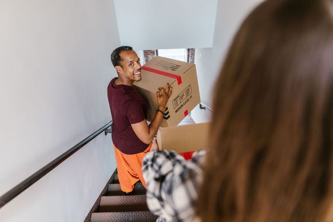 Person carrying cardboard boxes down a stairwell, with another person reaching from behind.