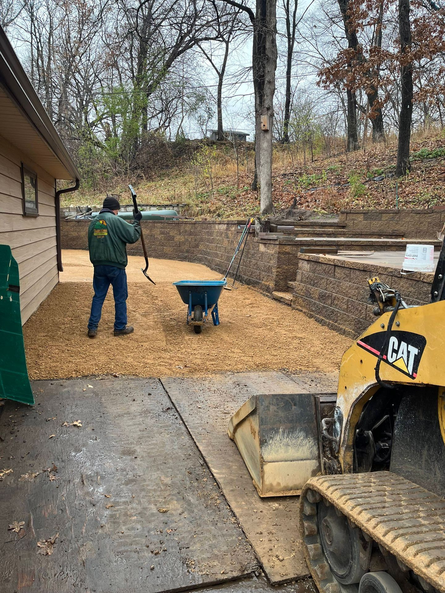 A man is pushing a wheelbarrow in a driveway next to a bulldozer.