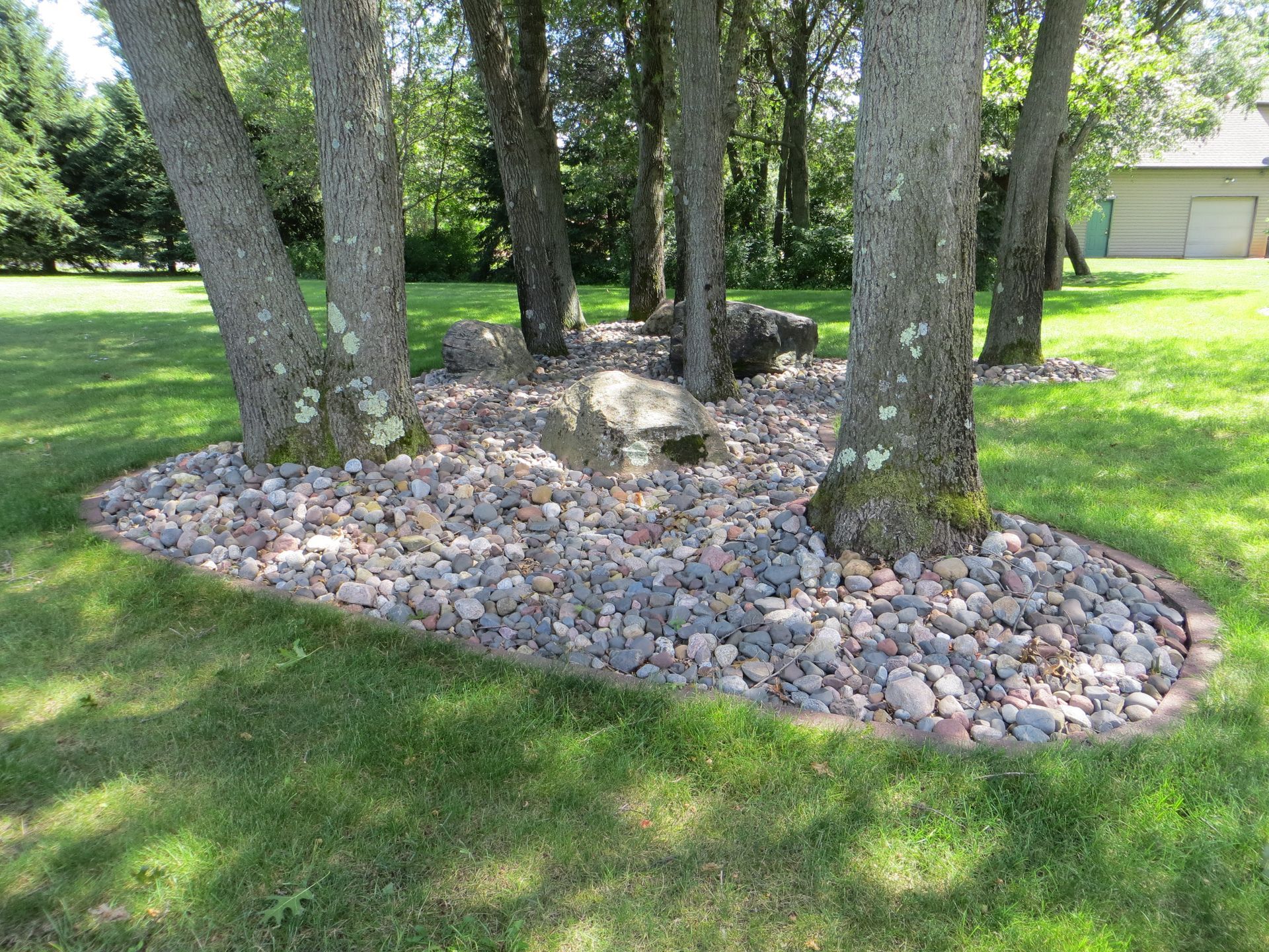 A tree surrounded by a rock garden in a yard with a garage in the background.