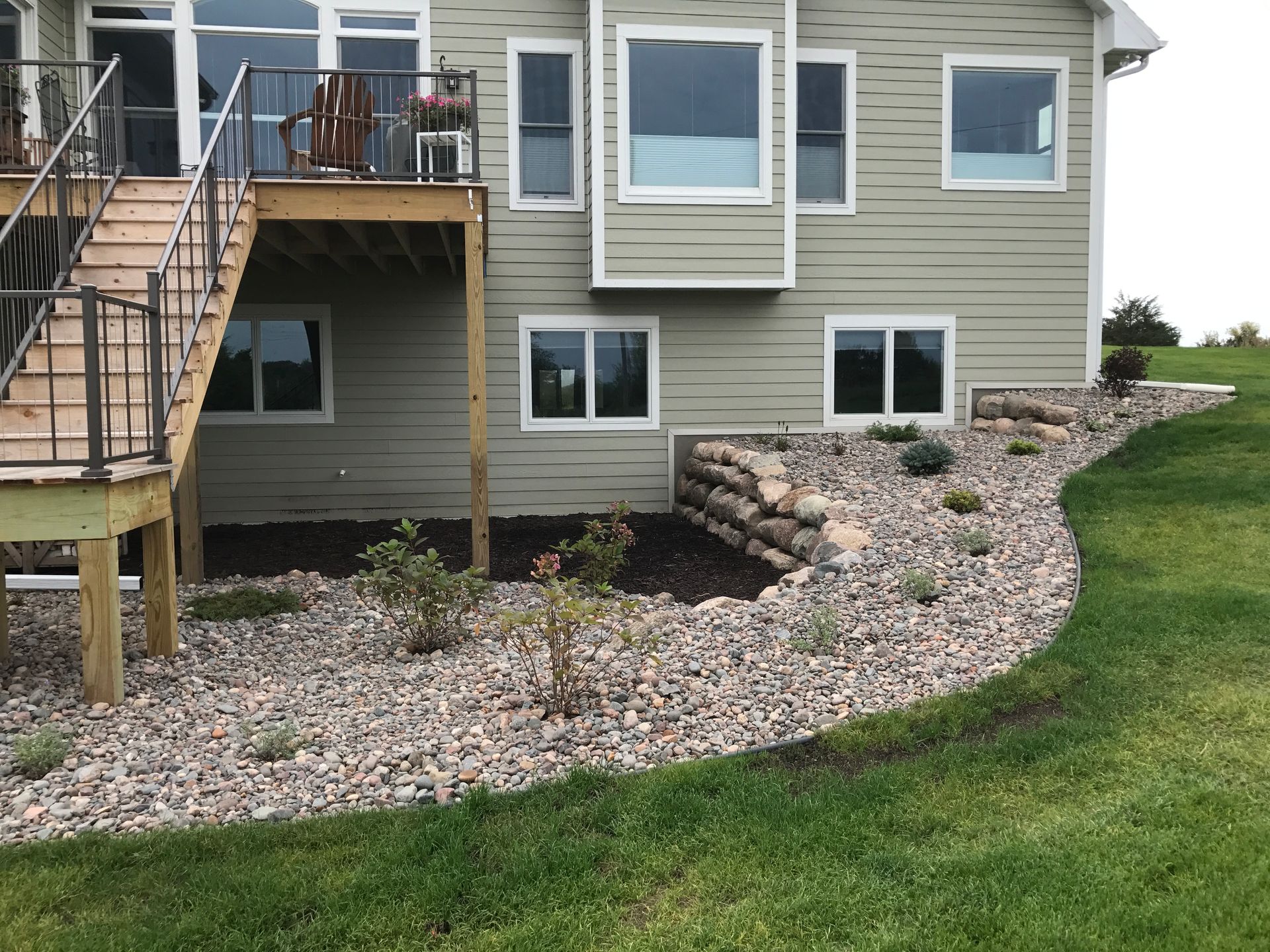 The back of a house with rock garden and retaining wall next to a deck and stairs. 