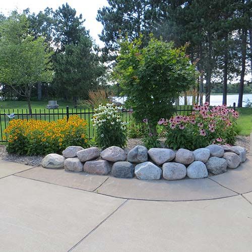 A garden with rocks and flowers in front of a lake